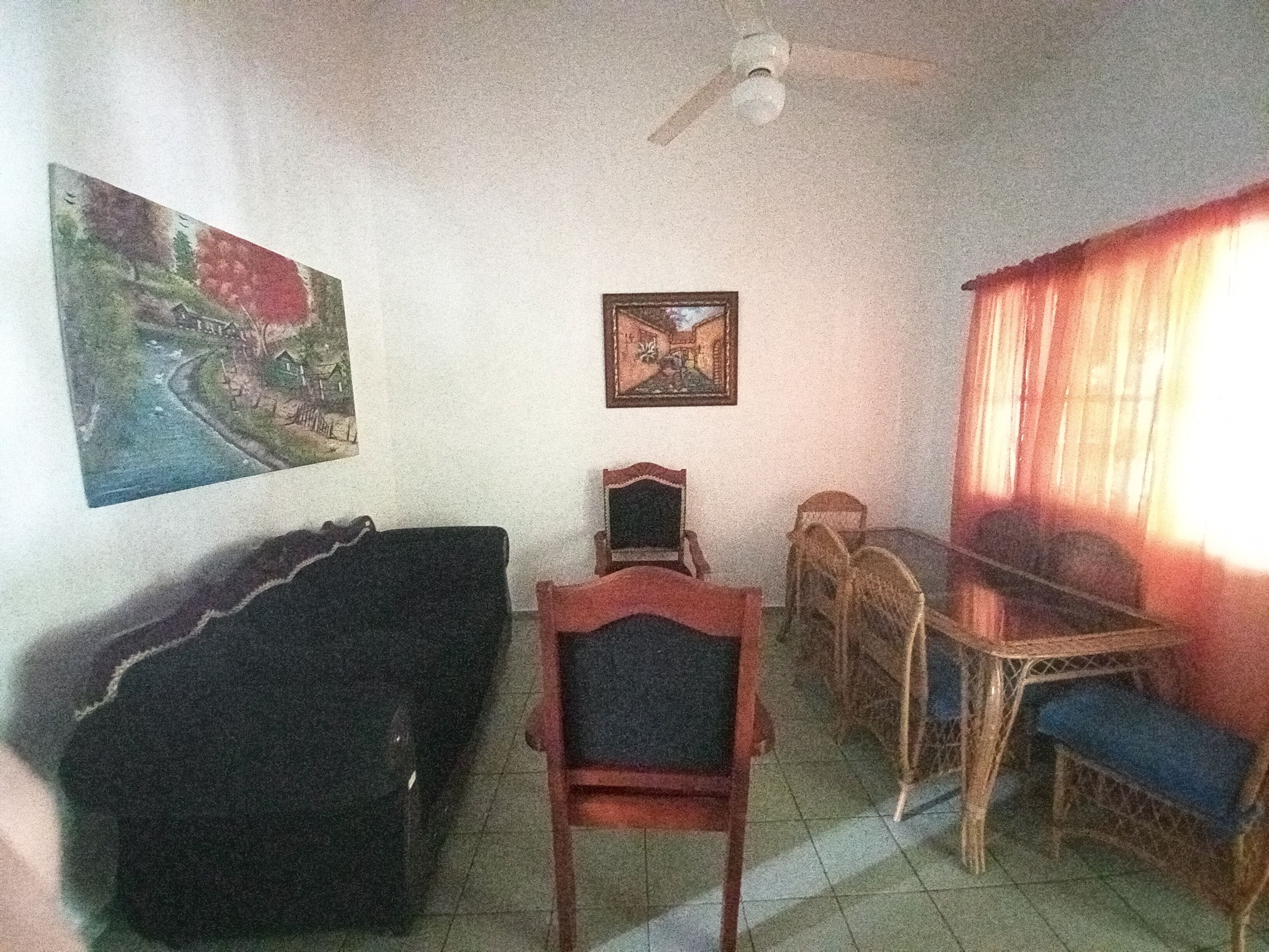 A dining area with a table and chairs, a ceiling fan, and two paintings on the wall.