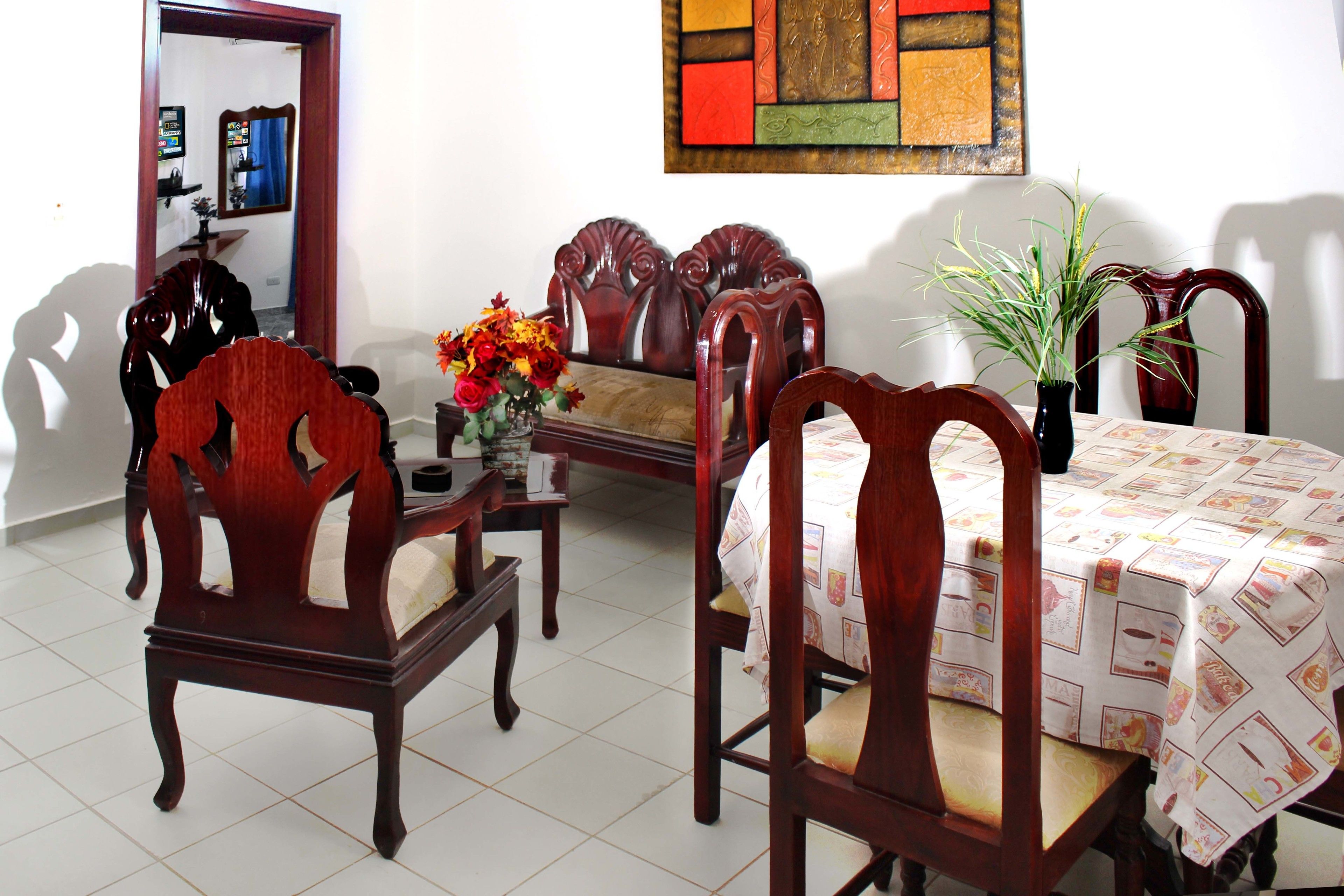 A dining area with a wooden table and chairs, a vase with flowers, and a mirror on the wall.