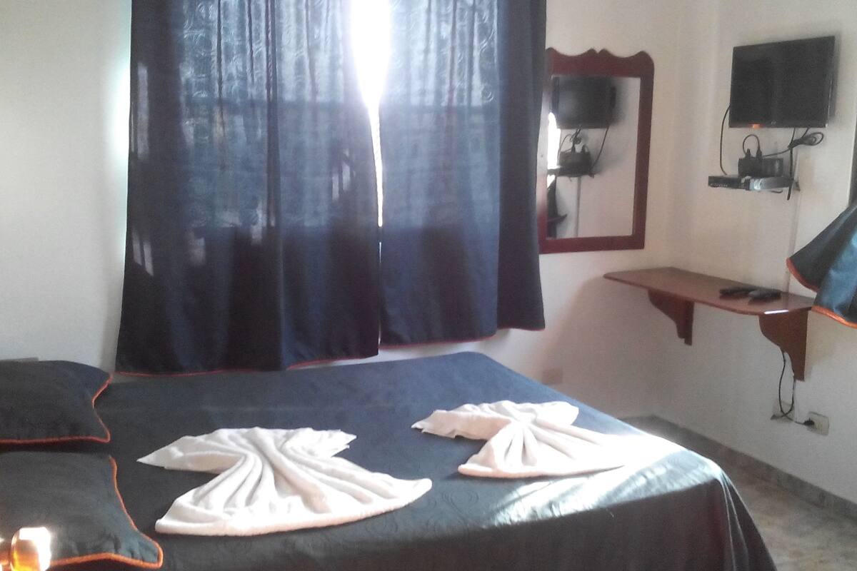 A bedroom with a bed, a bedside table, a mirror, and a TV mounted on the wall.