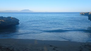 Une plage à l’eau d’un bleu limpide, bordée de formations rocheuses, avec une montagne qui se profile à l’horizon.