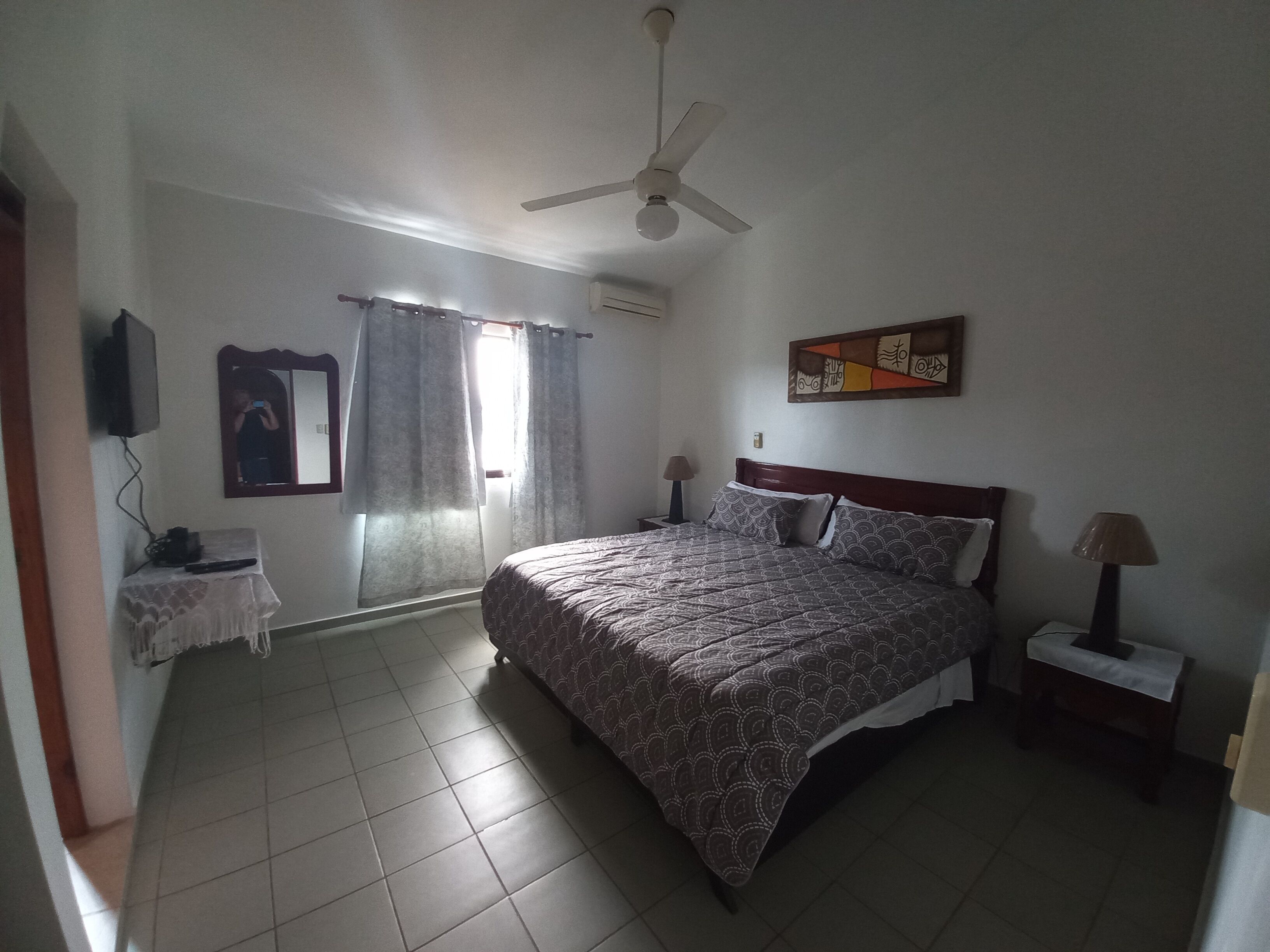 A bedroom with a bed, a ceiling fan, a painting, and a window with curtains.
