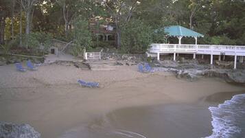 A beach with a white gazebo, blue lounge chairs, and a building with a green roof.