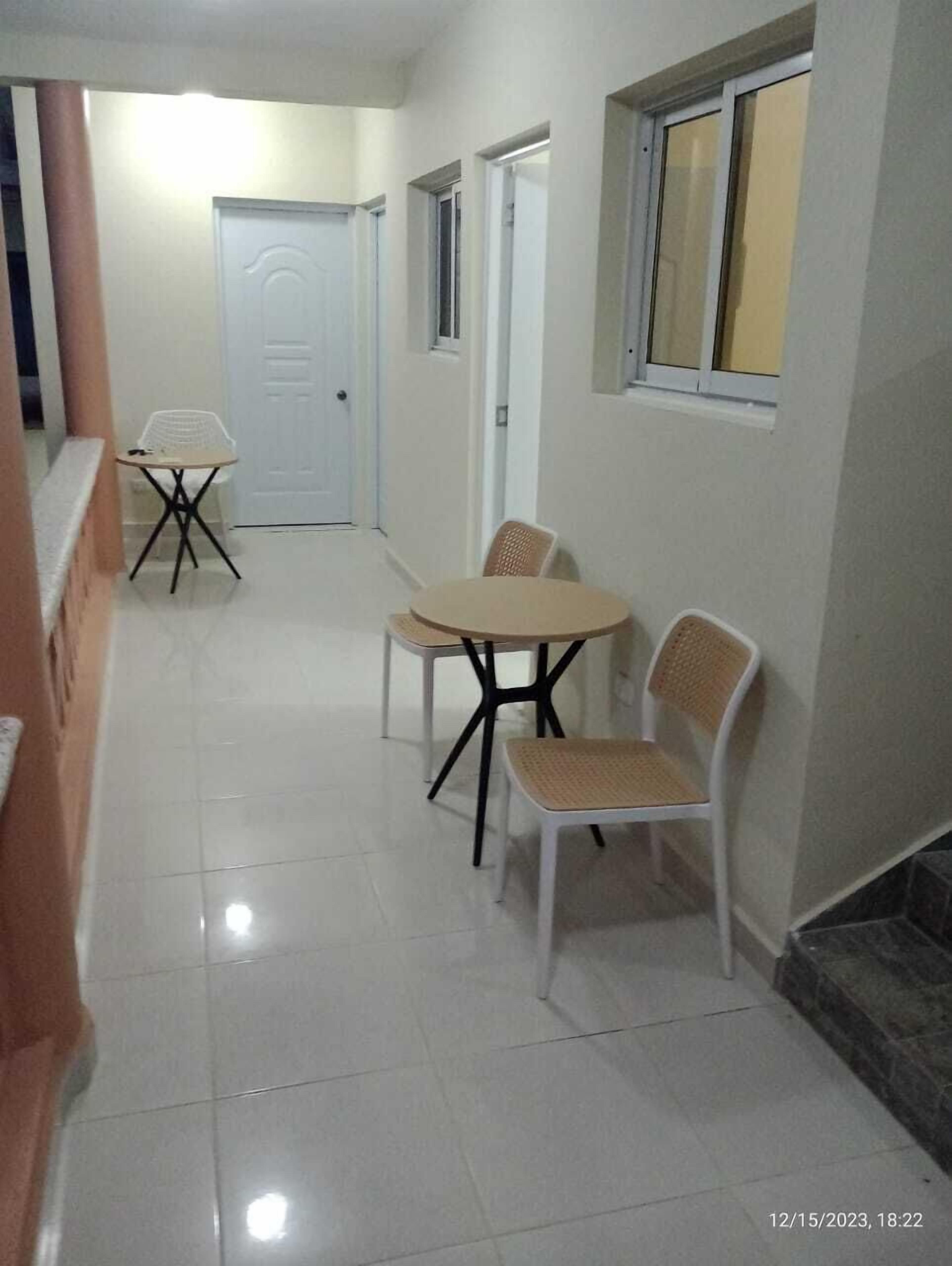 Un passadís net i ben il·luminat amb zona de menjador que presenta una taula rodona i quatre cadires. Hi ha portes blanques i una finestra a la paret dreta.