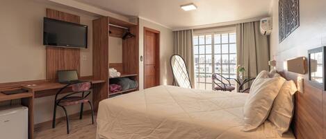 Habitación de hotel con cama, escritorio, silla, televisor y vistas a la ciudad.