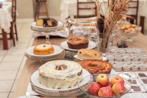 A buffet table with various baked goods, including cakes and pastries, and a bowl of apples. - Hotel Mont Blanc (Bento Gonçalves)