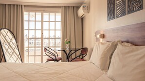 Habitación de hotel con una cama grande, una mesa con sillas, vista de la ciudad por una ventana y paneles decorativos en la pared.