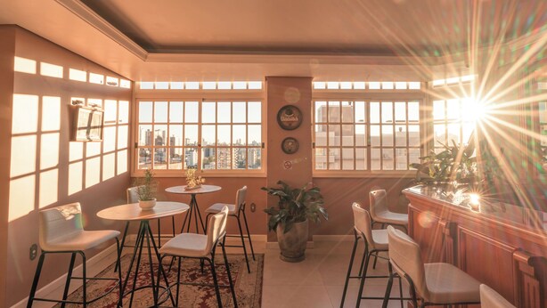 Una habitación soleada con ventanas amplias, una zona de bar y un comedor con sillas y una mesa.
