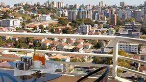 Un balcón con una mesa preparada para el desayuno, con vistas a un paisaje urbano que incluye edificios residenciales y comerciales.