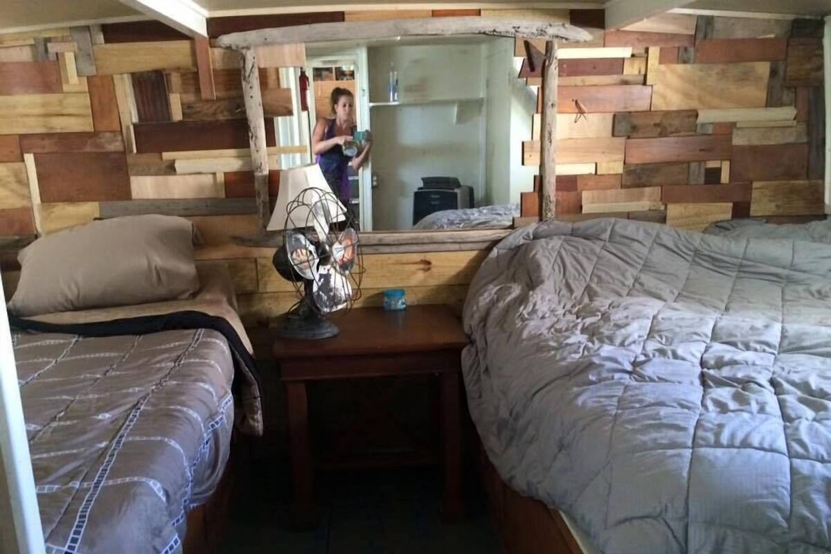 A compact room with two beds, a small table with a lamp, and a mirror on the wall.