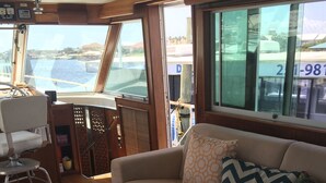 Ein gemütliches Interieur mit einer Couch, einem farbenfrohen Teppich und Blick auf das Wasser durch große Fenster.