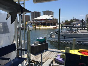 Uma marina com barcos atracados, um deck de madeira e um edifício com telhado branco ao fundo.