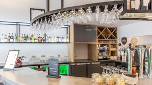 A bar area with a curved counter, hanging glasses, and a chalkboard sign. - Campanile PRIME - Metz Centre Gare (Metz)