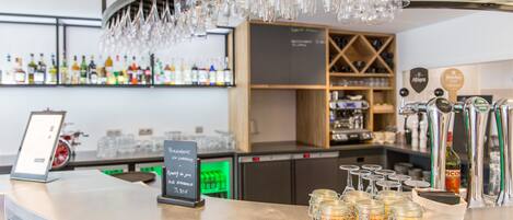 Un espace bar doté d’un comptoir incurvé, de verres suspendus et d’un panneau d’affichage en ardoise.