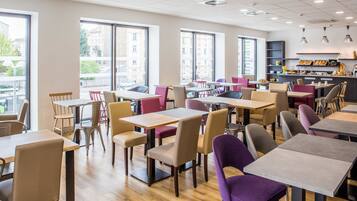 A modern cafe with multiple seating areas, including tables and chairs, and large windows providing views of the outside.
