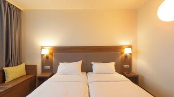 A hotel room with two beds, wooden headboards, bedside lamps, a nightstand with a remote control, and a yellow pillow.