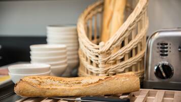 Una hogaza de pan sobre una tabla de cortar con un cuchillo, una cesta de barras y un tostador al fondo.