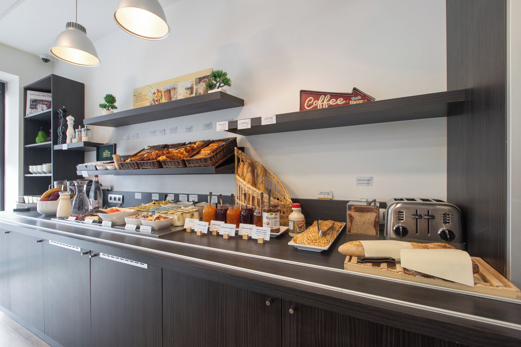 Una barra de desayuno con diversas opciones de comida, un cartel de café y un tostador.