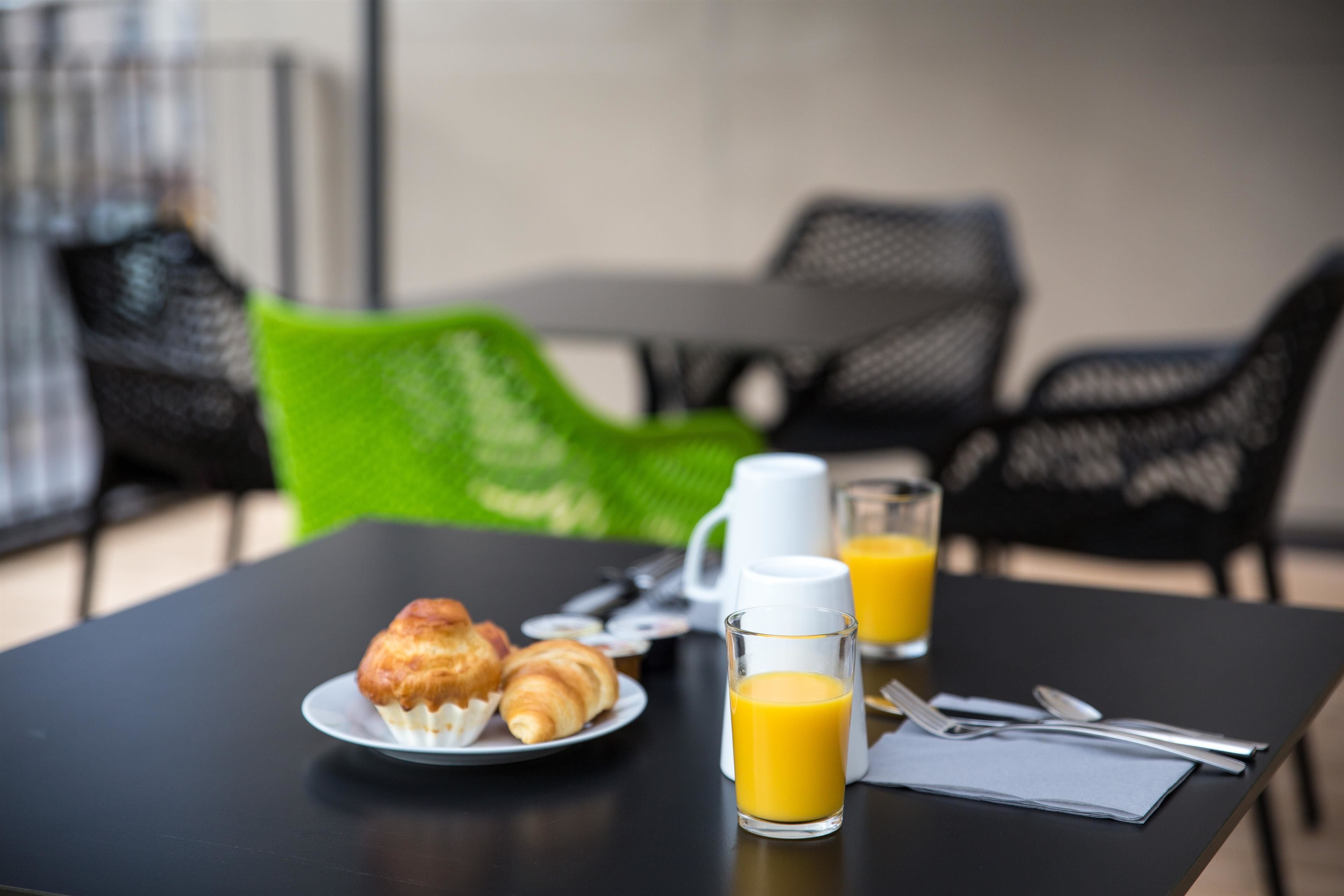 A breakfast table with croissants, a coffee pot, a glass of orange juice, and breakfast utensils.
