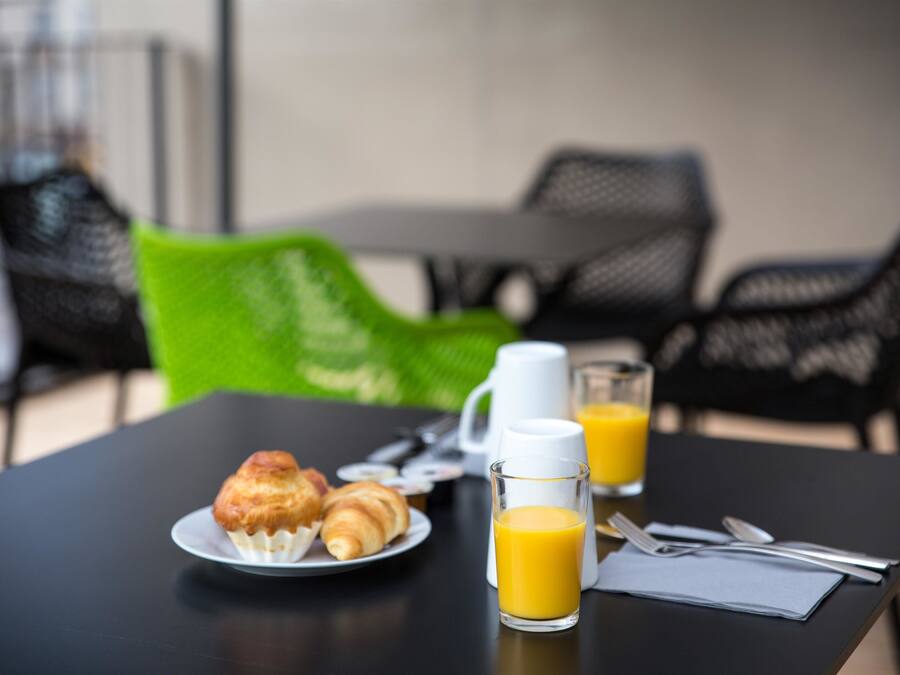 A breakfast table with croissants, a coffee pot, a glass of orange juice, and breakfast utensils.