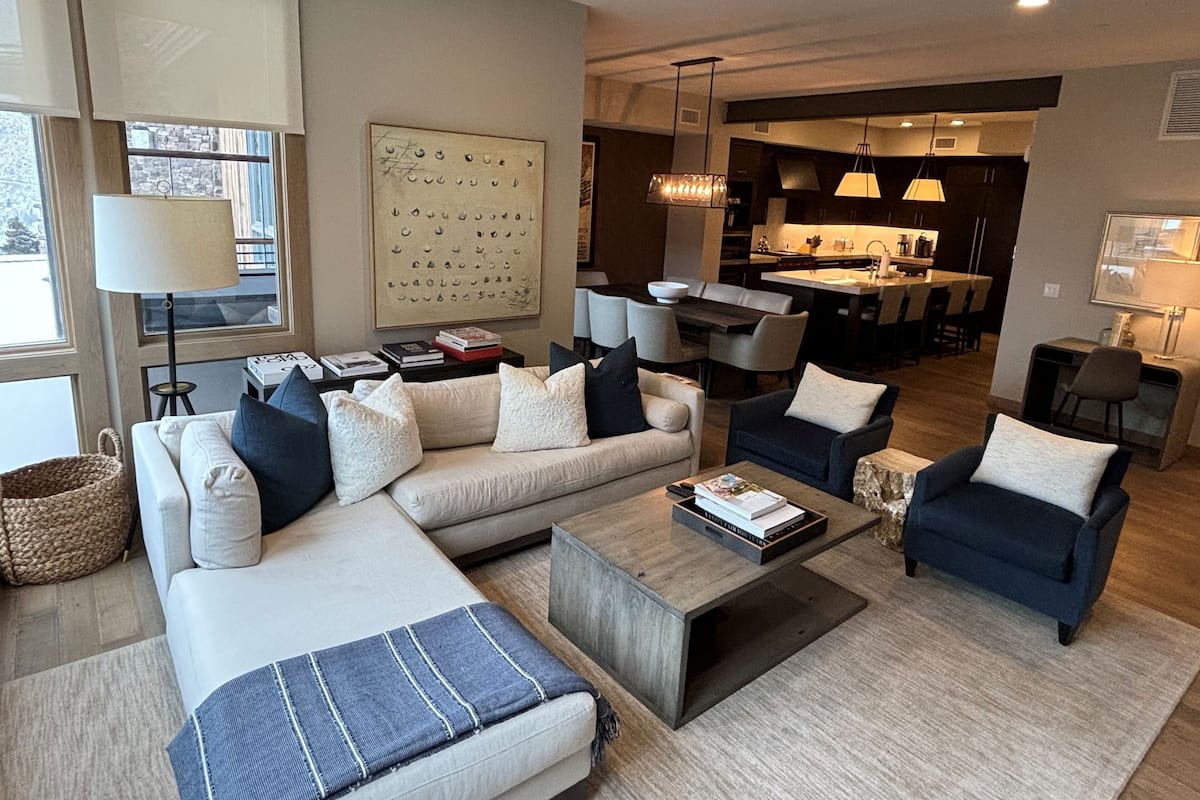 Een moderne woonkamer met een modulaire bank, een salontafel en een eethoek, met een keuken op de achtergrond.