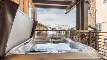 A hot tub in an outdoor setting with a wooden deck and stone wall.