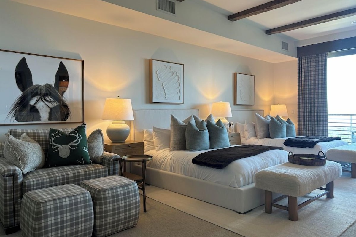 Un dormitorio moderno con una cama grande, dos mesitas de noche, un sofá y una silla. Hay lámparas de pared y cuadros enmarcados.