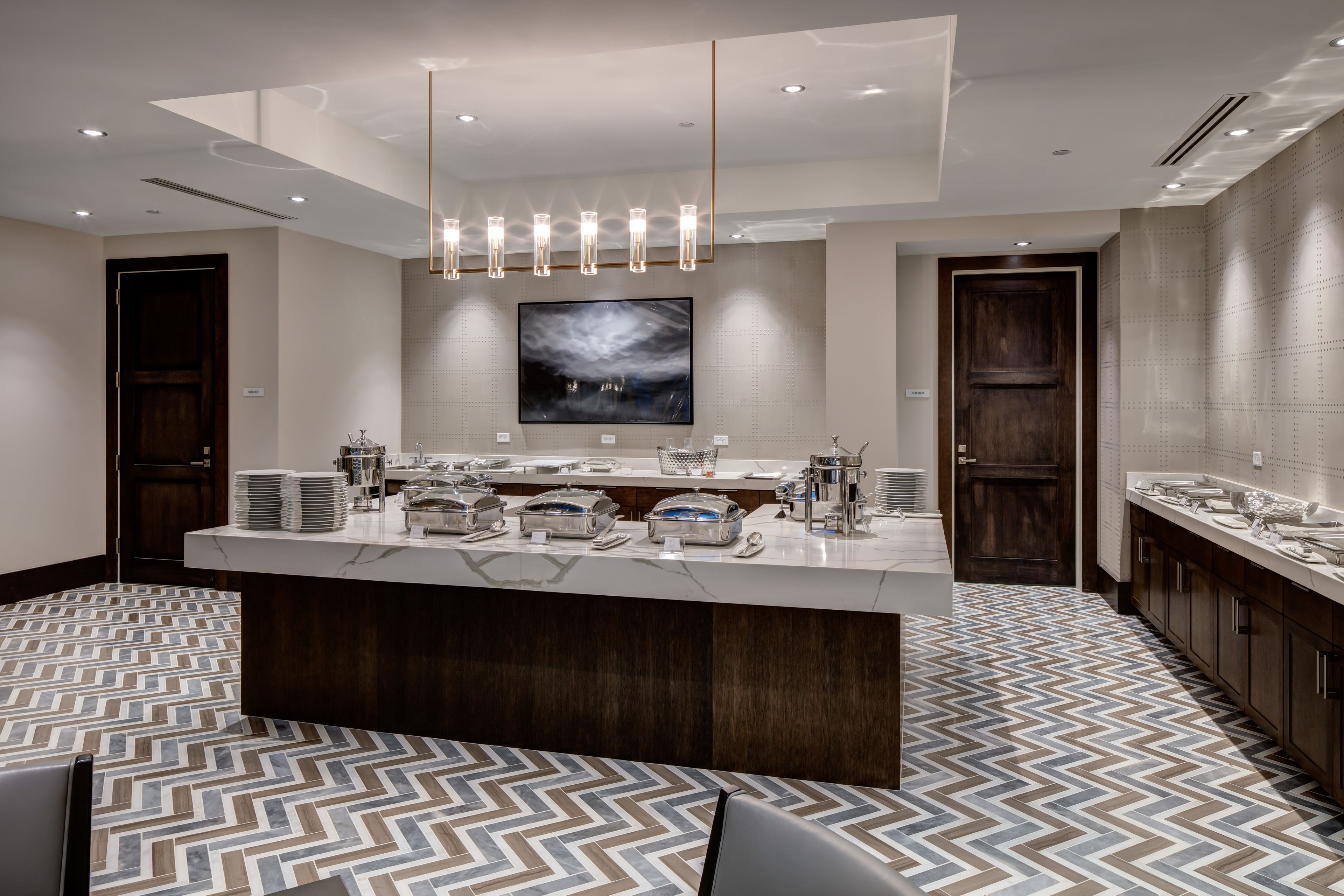 A modern hotel lobby with a central reception desk, a large abstract painting above the counter, and a patterned floor.