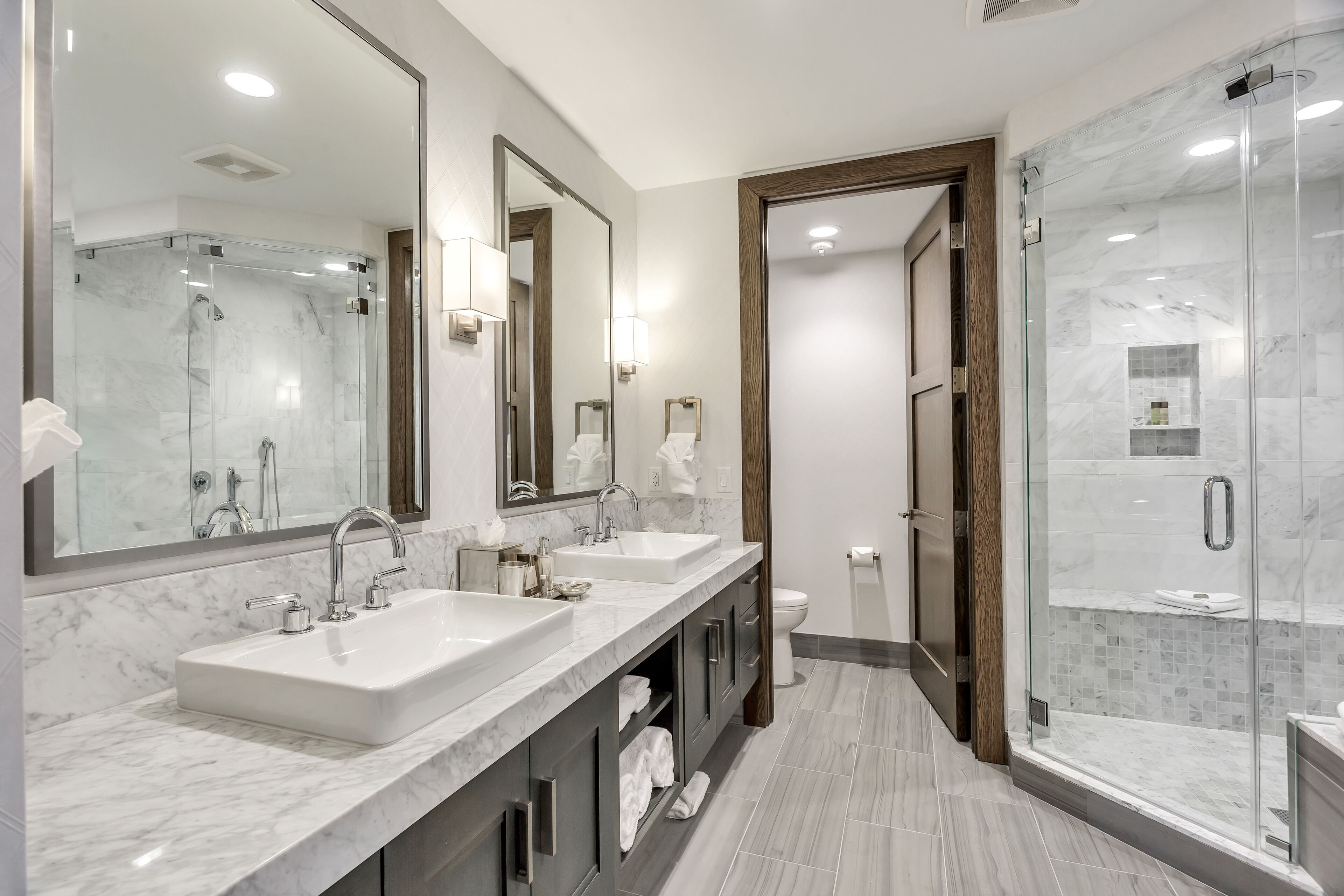 A modern bathroom with two sinks, a large mirror, and a glass-enclosed shower.