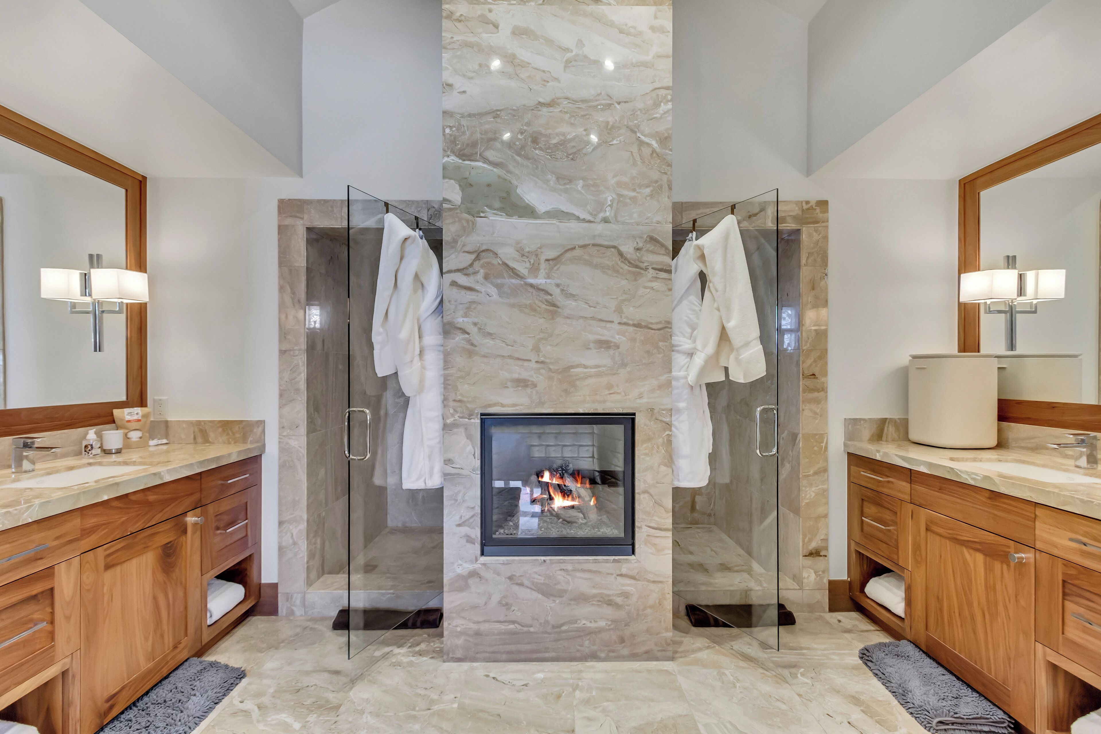 Un baño moderno con ducha de vidrio, pared de mármol, chimenea empotrada y muebles de madera.