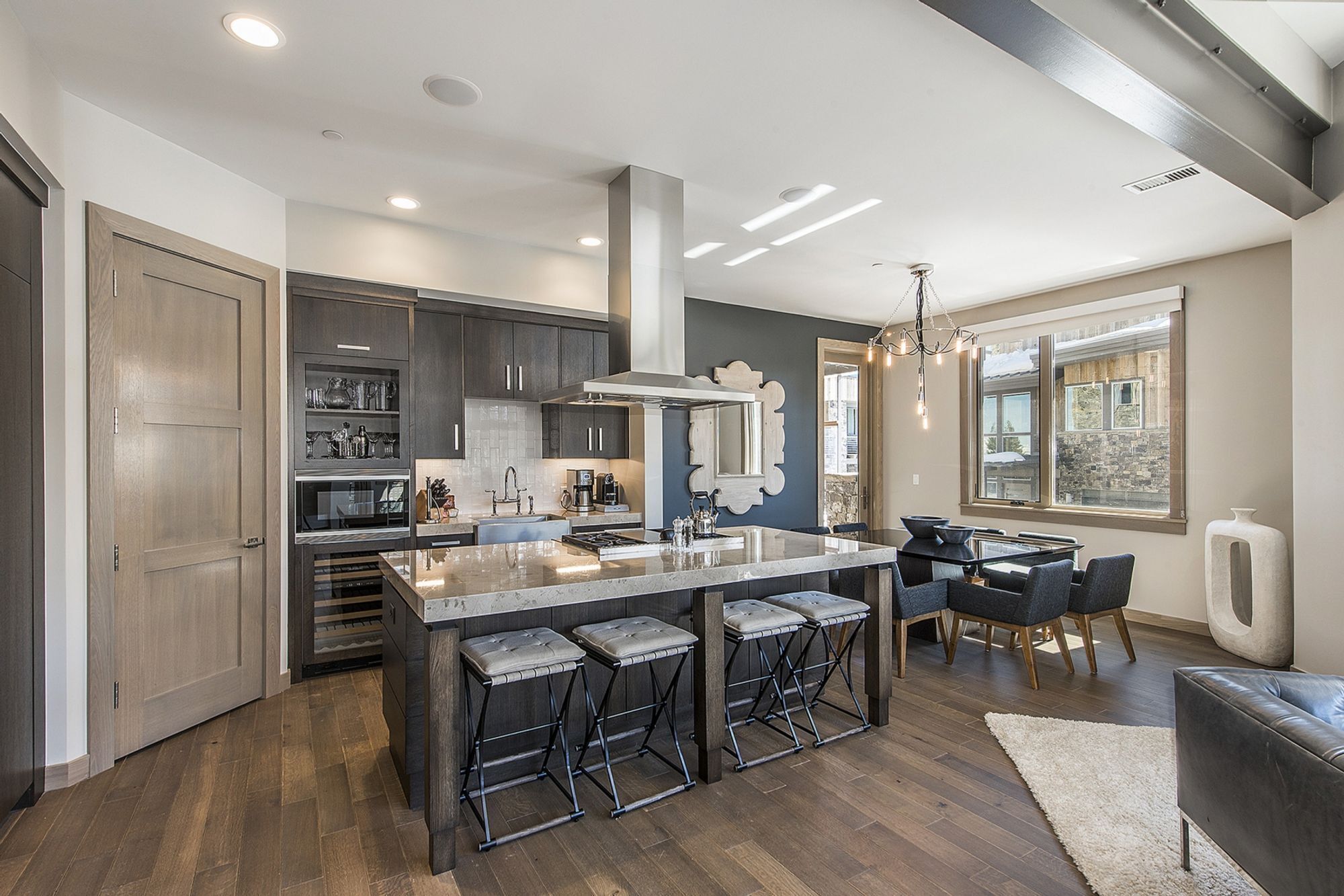 A modern kitchen with dark wood cabinets, a large island with bar stools, and a dining area with a chandelier.