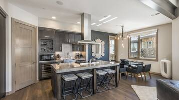 A modern kitchen with dark wood cabinets, a large island with bar stools, and a dining area with a chandelier.