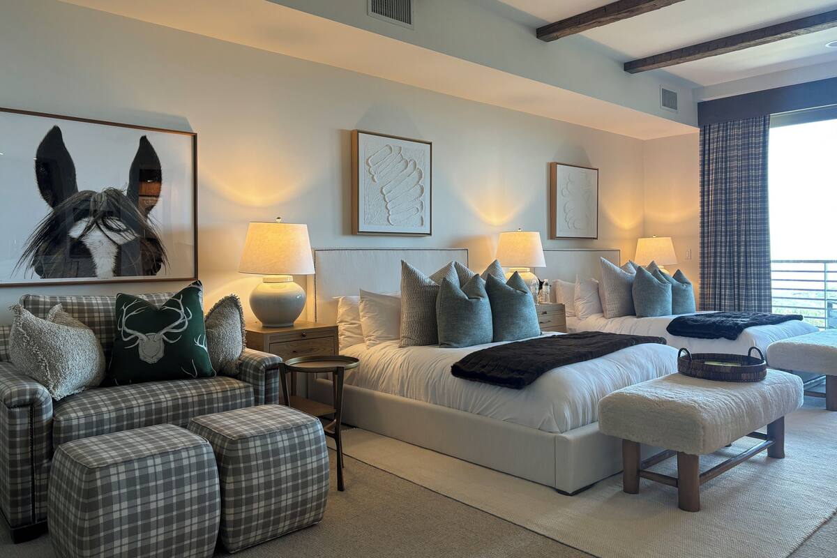 Une chambre moderne avec un grand lit, deux tables de chevet, un canapé et un banc. Le lit est garni de plusieurs oreillers et d’une couverture.