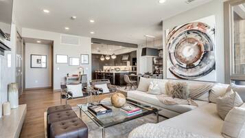 A spacious living room with a modern sofa, a glass coffee table, and a dining area in the background.