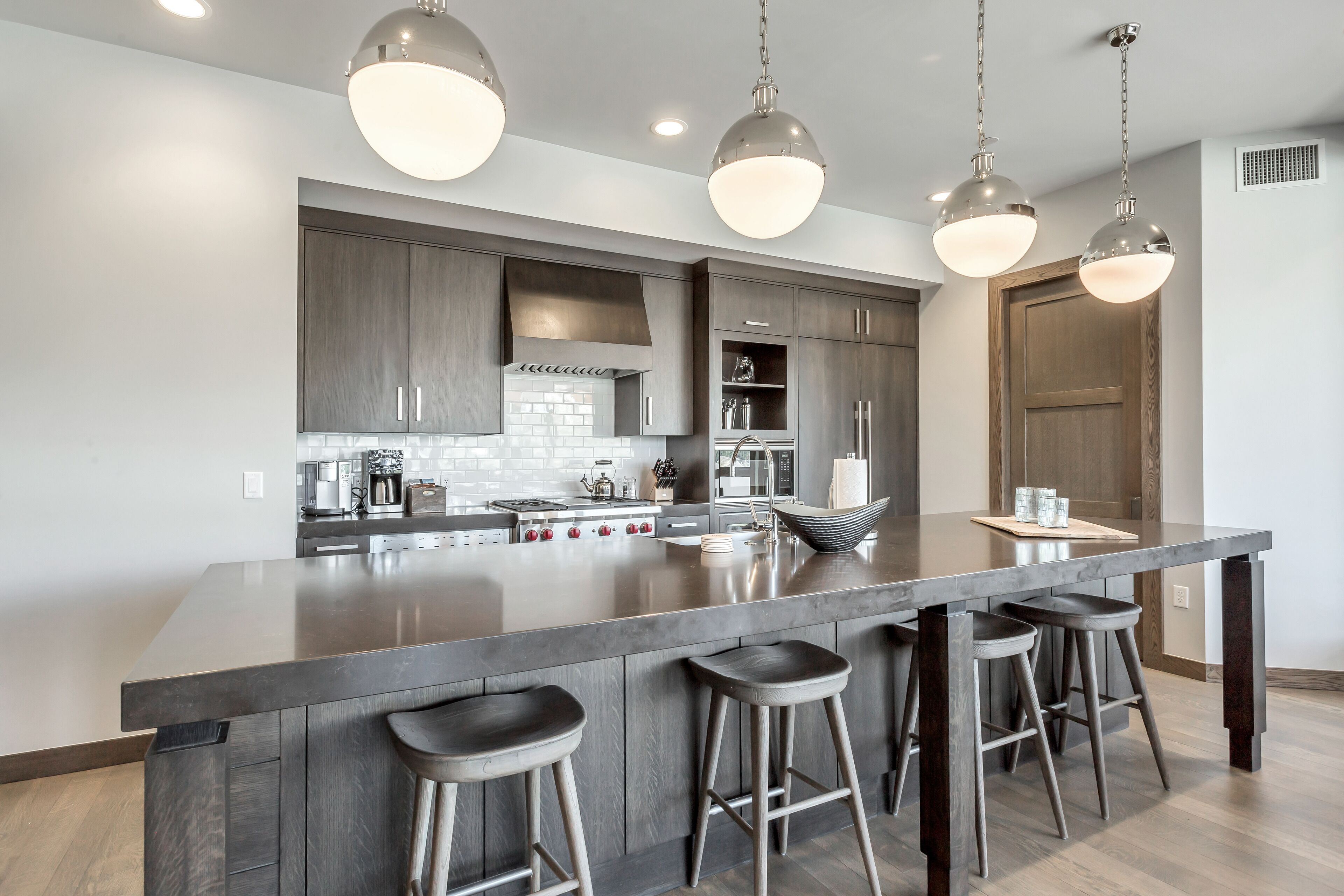 A modern kitchen with a large island, bar stools, pendant lighting, and built-in cabinetry.