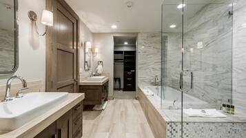 A modern bathroom with a large mirror, two sinks, a walk-in shower, and a walk-in closet.