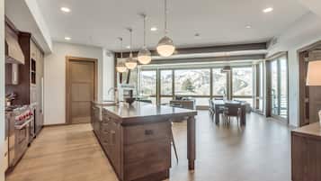 A modern kitchen with a central island, wooden cabinets, stainless steel appliances, and large windows offering a mountain view.
