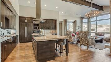 A modern kitchen with dark wood cabinets, a large island, and a dining area with patterned chairs.