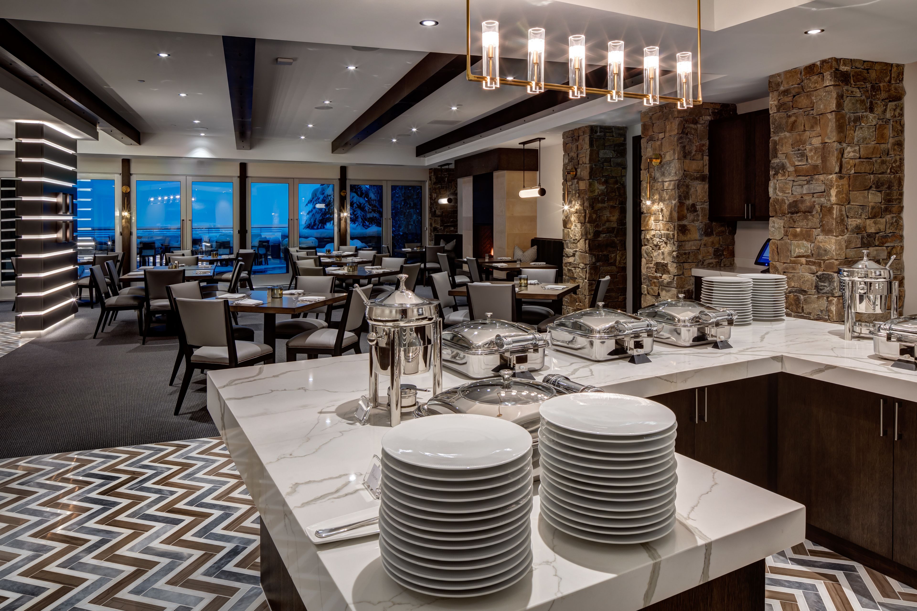 A modern dining area with marble countertops, stacked plates, and a stone accent wall.