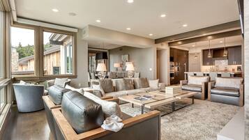 A spacious living room with a large sofa set, a coffee table, and a dining area with a kitchen in the background.