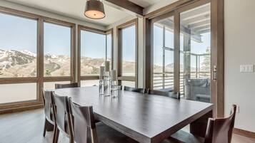 A dining area with a large table and chairs, large windows with a view of a mountainous landscape, and pendant lighting.