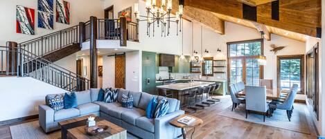 A spacious living area with a large sofa, coffee table, and a dining area with chairs. A staircase leads to an upper level.