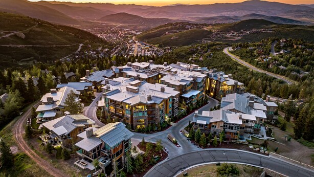 Un área residencial moderna con casas conectadas, grandes ventanales y paneles solares, rodeada de vegetación exuberante y un camino sinuoso.