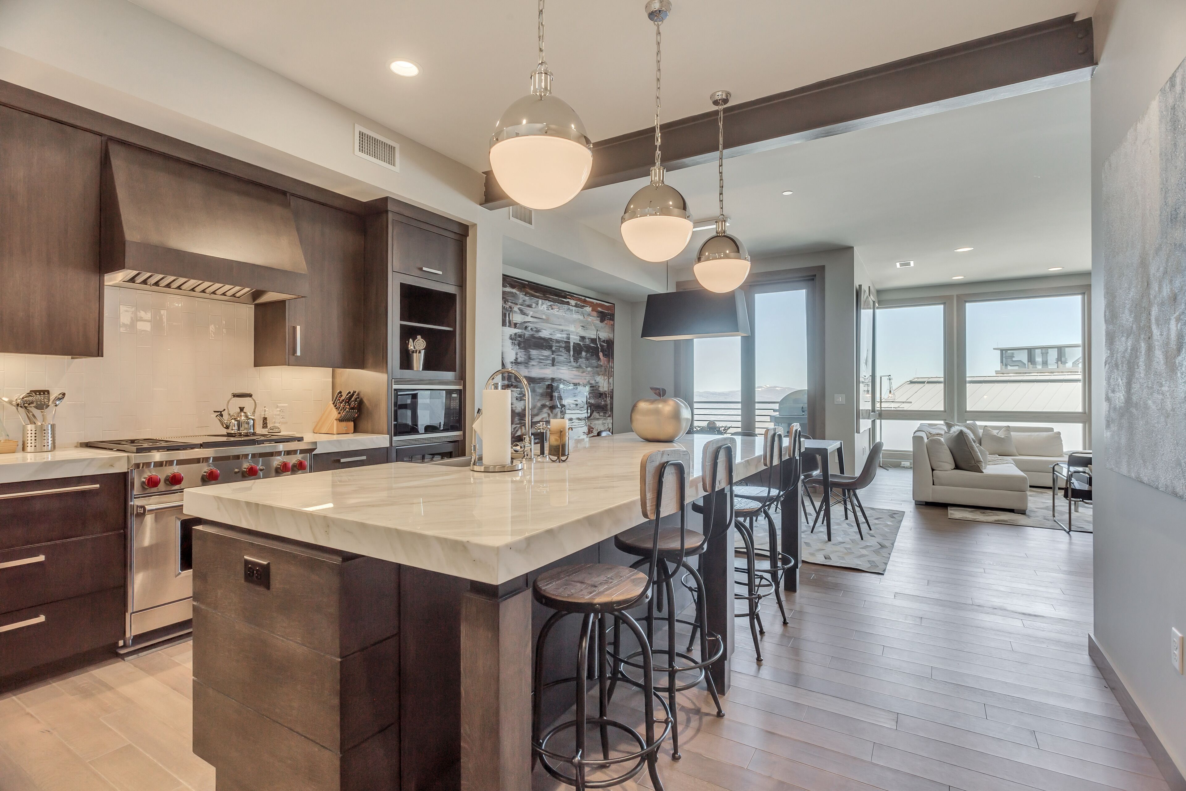 A modern kitchen with a large island, bar stools, and a dining area with a sofa and table.