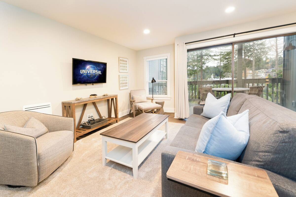 A modern living room with a grey sofa, a white coffee table, and a TV mounted on the wall.