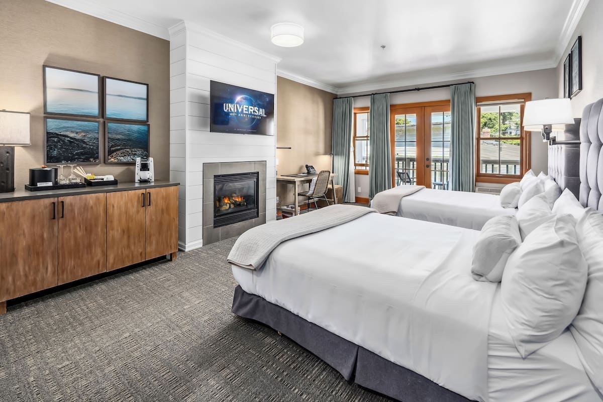 A hotel room with a large bed, a desk, a fireplace, and a TV mounted on the wall.