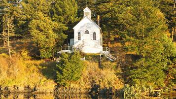 Uma igreja branca com um campanário, rodeada por árvores densas e refletida em águas calmas.