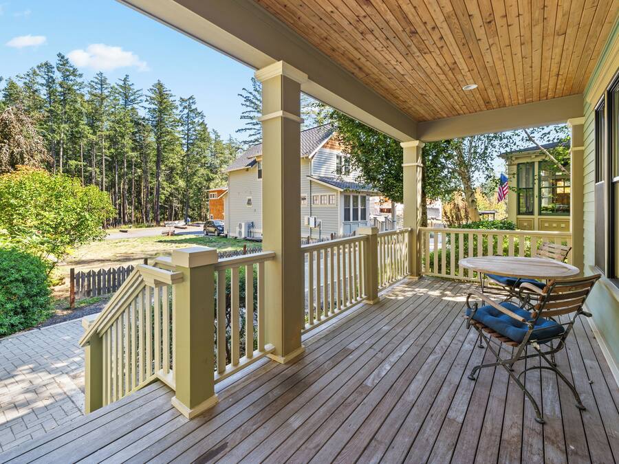 A wooden deck with a table and chairs, surrounded by a railing, overlooking a residential area with houses and trees.