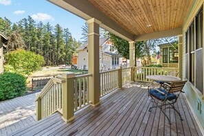 A wooden deck with a table and chairs, surrounded by a railing, overlooking a residential area with houses and trees.