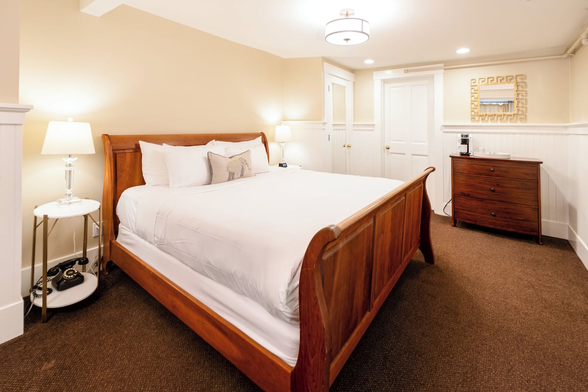 A neatly arranged bedroom with a large wooden bed, bedside lamps, a dresser, and a door leading to another room.