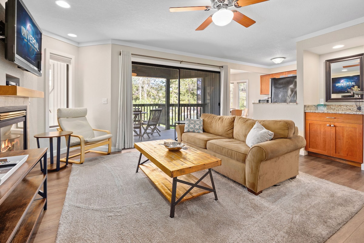 A living room with a wooden coffee table, beige sofa, and a TV mounted on the wall.